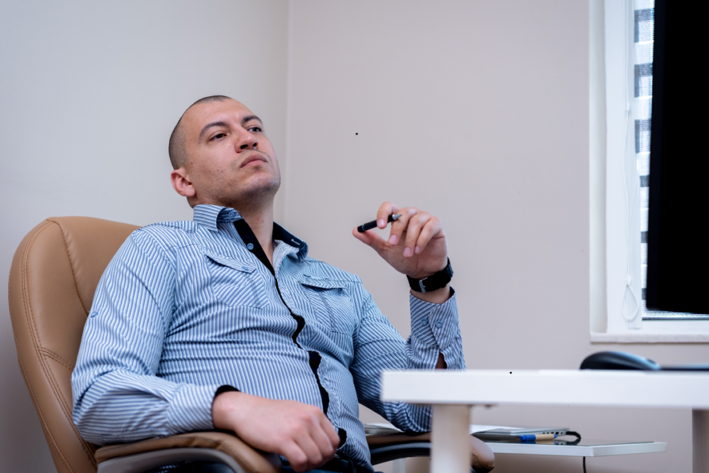 A professional man seated in an office chair, wearing a Calvin Klein style CJMW2466 pinstripe shirt, exuding a confident and focused demeanor.