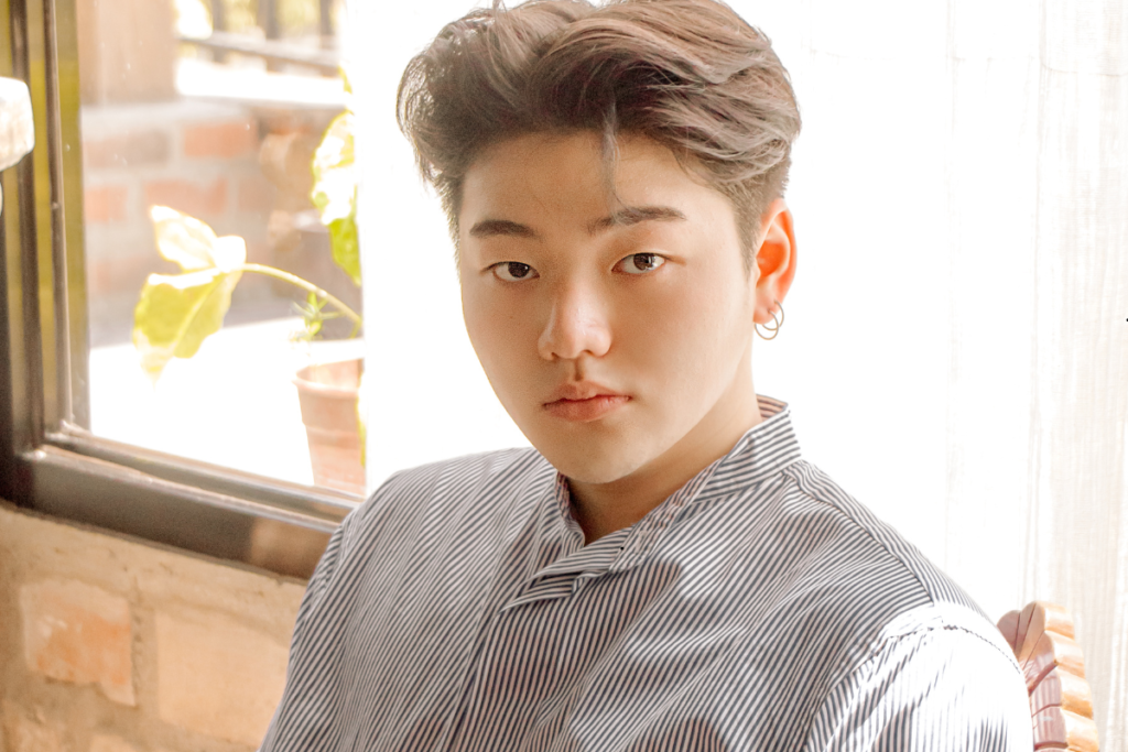 A stylish man wearing a Calvin Klein style CJMW2466 pinstripe shirt, sitting in a naturally lit room.